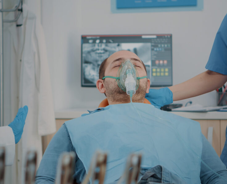 Patient with oxygen mask receiving anesthesic in dentistry cabinet, getting ready for stomatological procedure with dental tools and drill to polish caries. Oral care anesthesia on man.