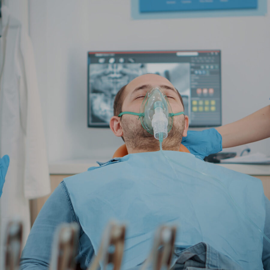 Patient with oxygen mask receiving anesthesic in dentistry cabinet, getting ready for stomatological procedure with dental tools and drill to polish caries. Oral care anesthesia on man.